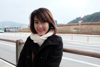 Portrait of smiling young woman standing on road against sky