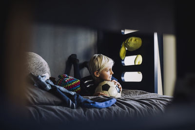 Boy with soccer ball looking away while lying on bed