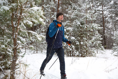 Skier with a backpack and hat with pompom with ski poles in his hands on background of a snowy 