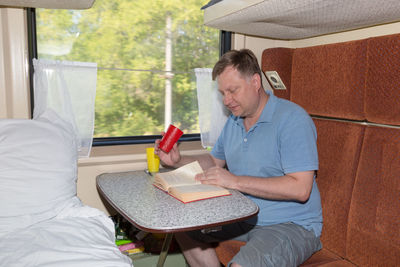 Adult blond man sitting in his train compartment, drinking tea, going on holiday.