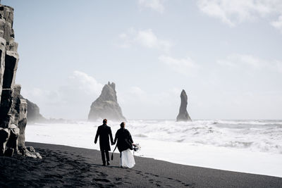 Rear view of people on beach against sky