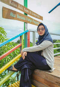 Portrait of young woman sitting on wooden wall