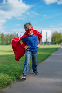 Full length of boy in superman costume walking on road against sky