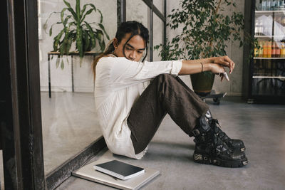 Full length side view of young non-binary professional sitting depressed at office