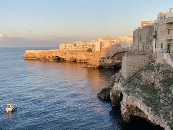 Buildings by sea against sky during sunset