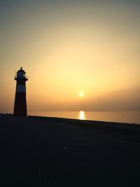 Silhouette lighthouse by sea against clear sky during sunset