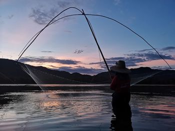 Man fishing in lake against sky during sunset