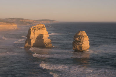 Rock formation in sea against sky during sunset