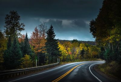 Country road by trees against sky during autumn