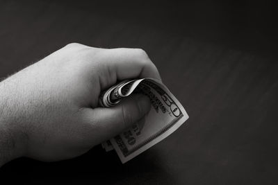 Cropped hand of person holding bitcoin against black background