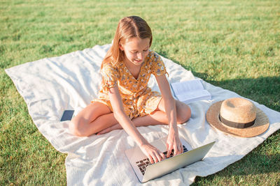 Smiling girl using laptop while sitting on grass at park