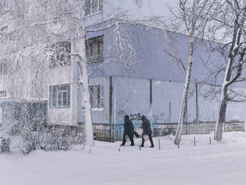 Rear view of people walking by building on snow 