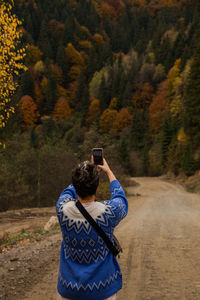 Rear view of person photographing through mobile phone in forest