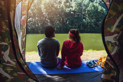 Rear view of people sitting on mat by lake