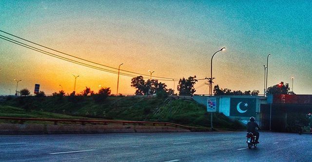 transportation, road, sky, land vehicle, bicycle, mode of transport, street, power line, electricity pylon, sunset, road sign, tree, the way forward, blue, street light, outdoors, on the move, country road, dusk, cable