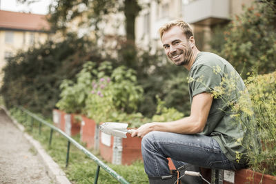 Side view portrait of happy man with shovel sitting in garden