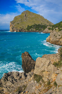 Scenic view of rocks by sea against blue sky