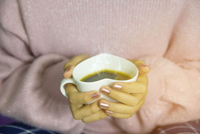 Midsection of woman holding heart shape coffee cup at home