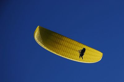 Low angle view of people paragliding against clear blue sky