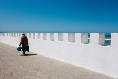 Rear view of woman walking on street against clear blue sky