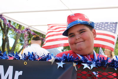 Smiling boy looking away while standing against american flag during event