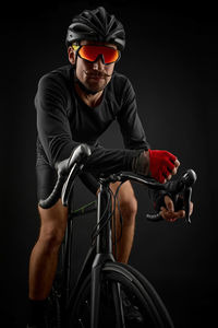 Athlete sitting on bicycle against black background