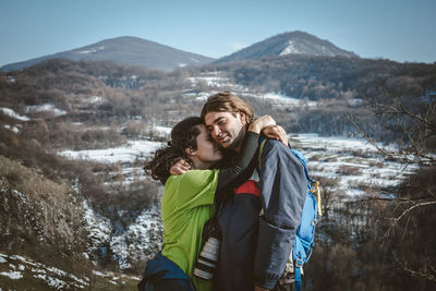 Couple embracing while standing on mountains against sky