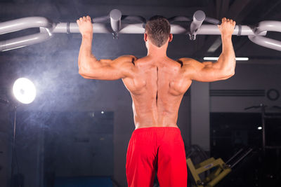 Rear view of shirtless man exercising at gym