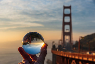Cropped image of hand holding crystal ball against sky during sunset