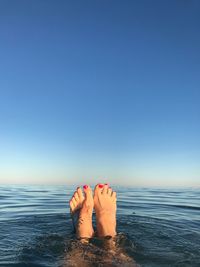 Low section of woman on sea against clear sky