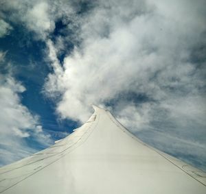 Cropped image of aircraft wing against cloudy sky