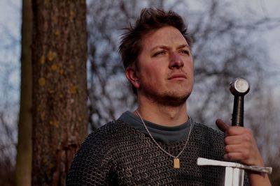 Portrait of man looking away against tree trunk