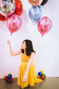 Full length of a young woman playing with balloons against white background