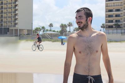 Full length of shirtless man smiling against sky