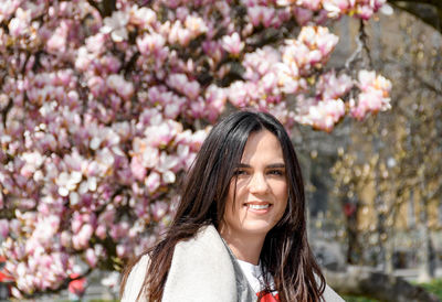 Portrait of beautiful young woman in front of pink magnolia tree.