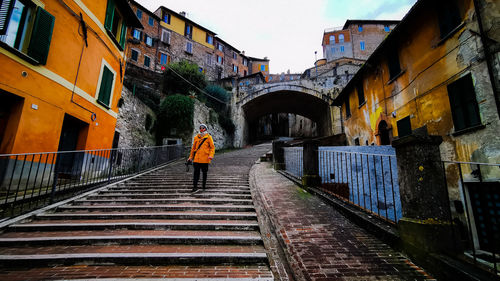 Rear view of man walking on staircase amidst buildings in city