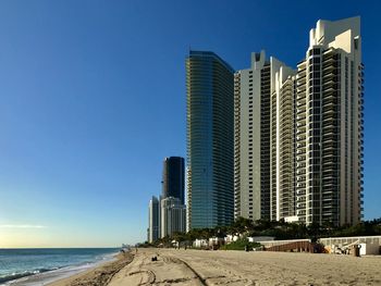 Modern buildings by sea against clear blue sky