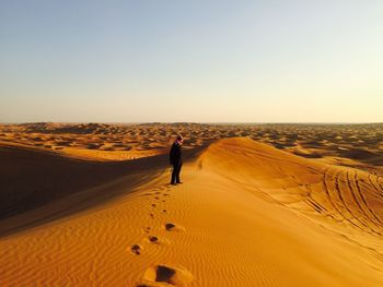 Man standing on sand dune against clear sky at desert