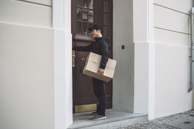 Full length of delivery man with package standing at doorstep