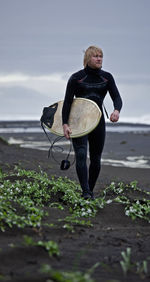 Young man walks with surfboard along beach in iceland