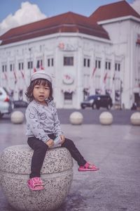 Portrait of cute girl sitting on seat in city