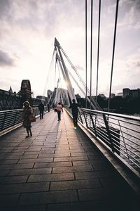 People walking on footbridge in city against sky