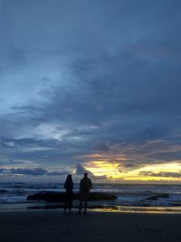 Silhouette men on beach against sky during sunset