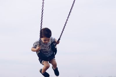Full length of boy playing on swing against sky