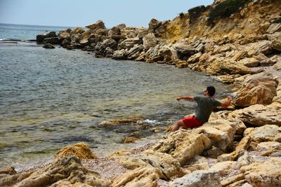 Man standing on rock at beach against sky