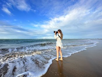 Full length of woman standing at beach against sky