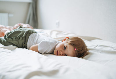 Cute funny baby girl in home clothes lies on bed at home