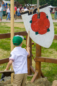 Rear view of boy holding wood against fence