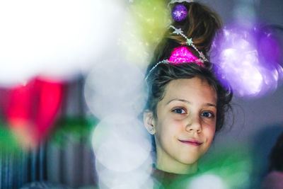 Close-up portrait of smiling girl by illuminated christmas lights