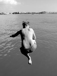 Rear view of shirtless boy jumping in lake against sky